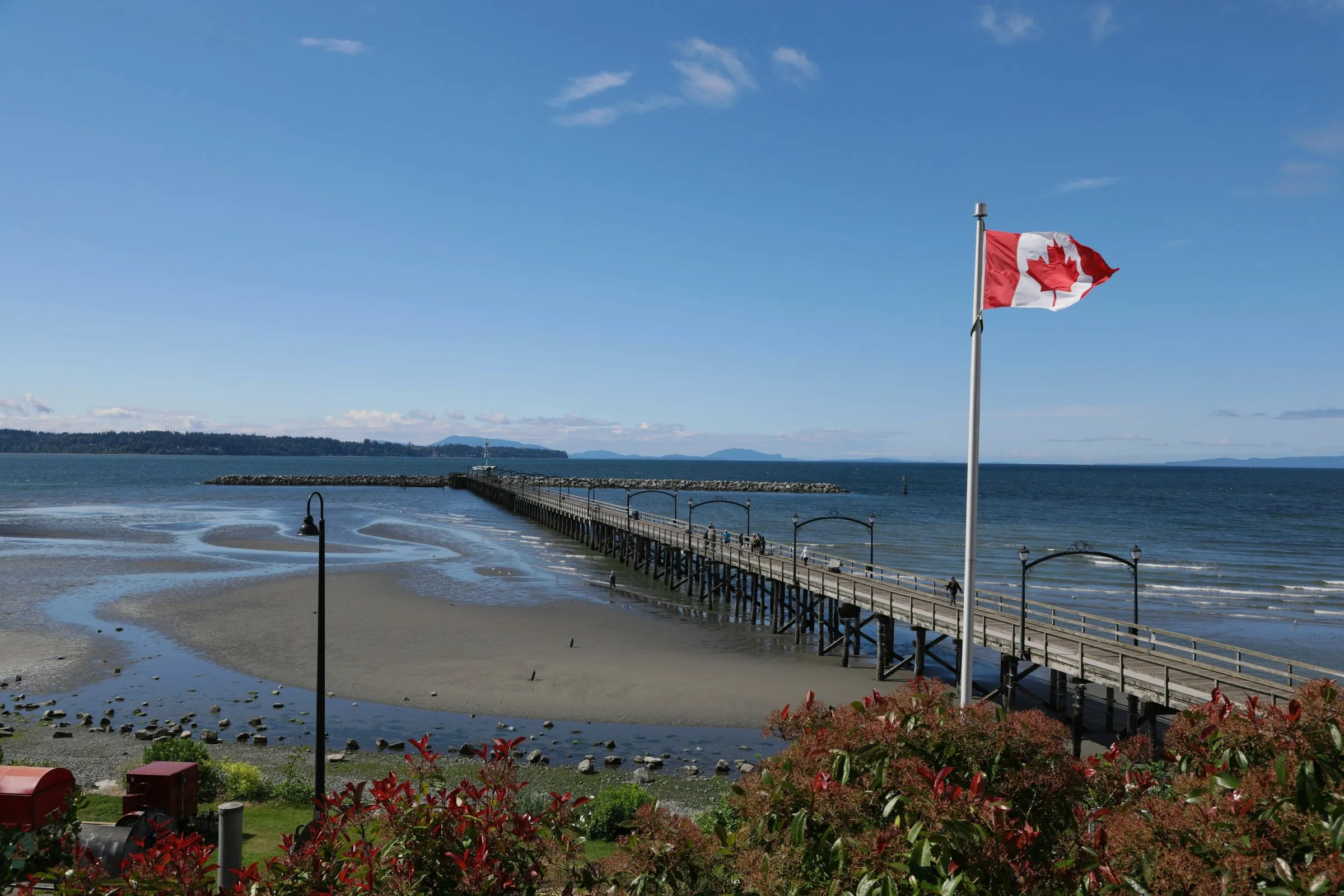 White Rock Pier stretching across the tidal flats, with a Canadian flag flying over the waterfront.
